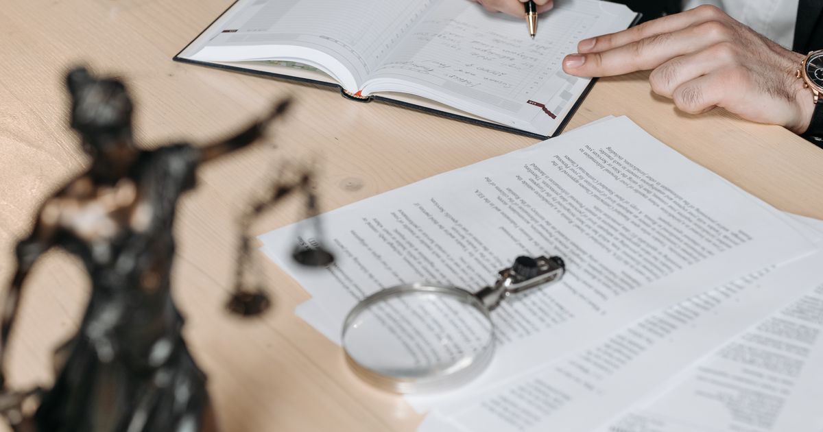 Expediente y documentos sobre un escritorio, junto a una lupa y una figura de la Justicia